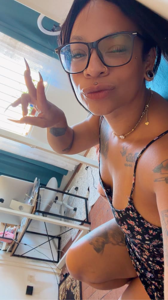 Woman with glasses and tattoos taking a playful selfie at home